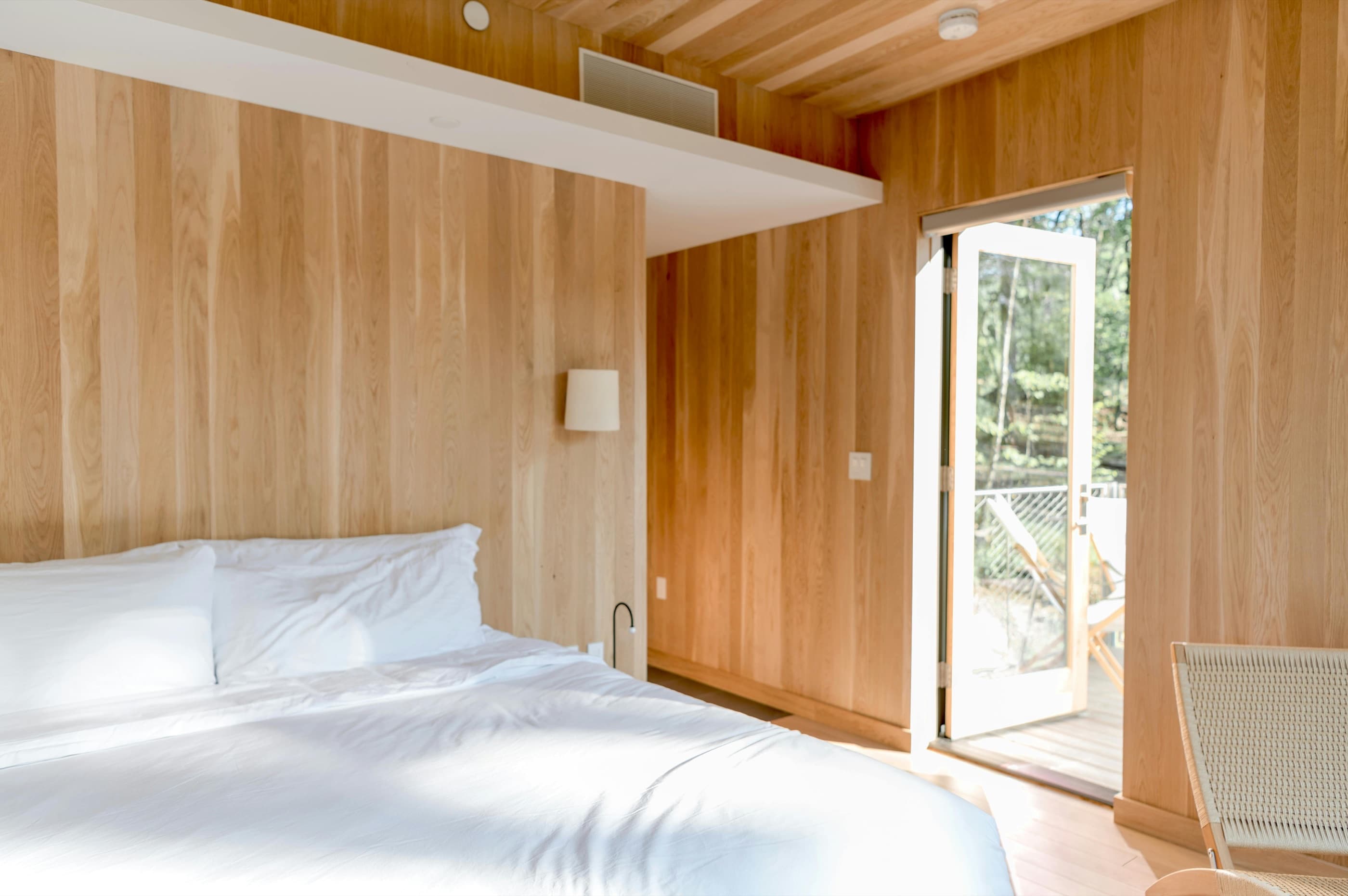 Chambre aux murs en bois clair, linge blanc et porte ouverte sur la nature